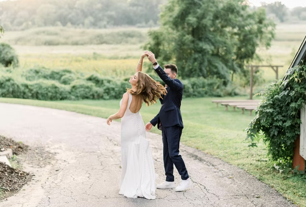 A groom twirling his bride along a gravel path with greenery all around.